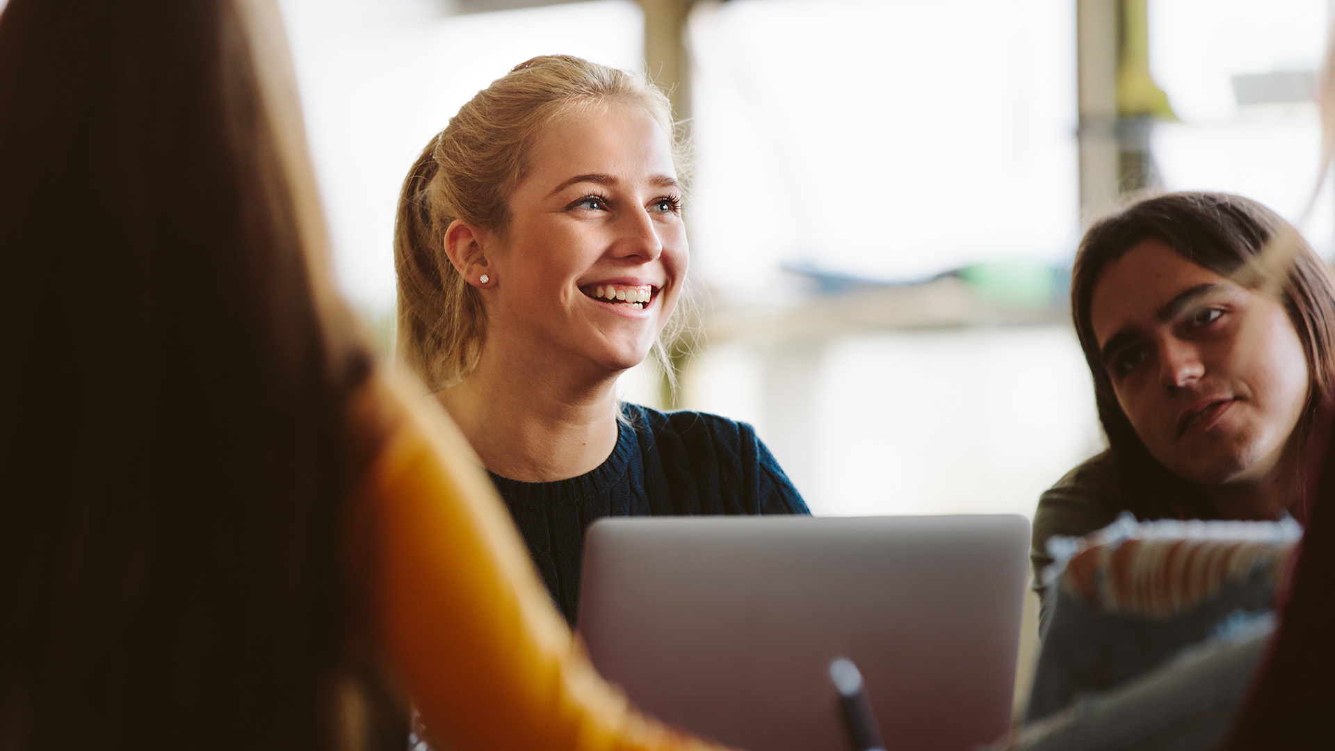 Iloinen nuori opiskelija ryhmätyössä kannettavan tietokoneen äärellä.