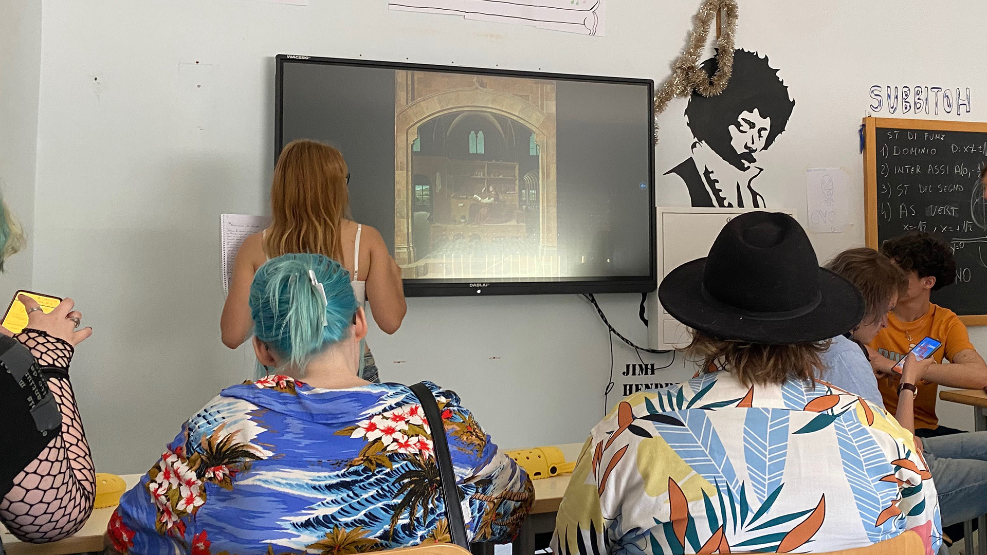 Taideluokassa opetusta, jossa värikkäästi pukeutuneet opiskelijat on kuvattu takaapäin.