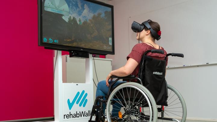 Henkilö pyörätuolissa ja virtuaalilasit päässä kuntoutumassa RehabWall -laitteella