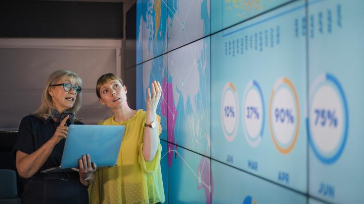 Kaksi naista katsoo tietoja suurelta data-screeniltä