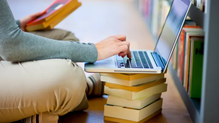 asiakas istumassa lattialla kannettava tietokone kirjapinon päällä