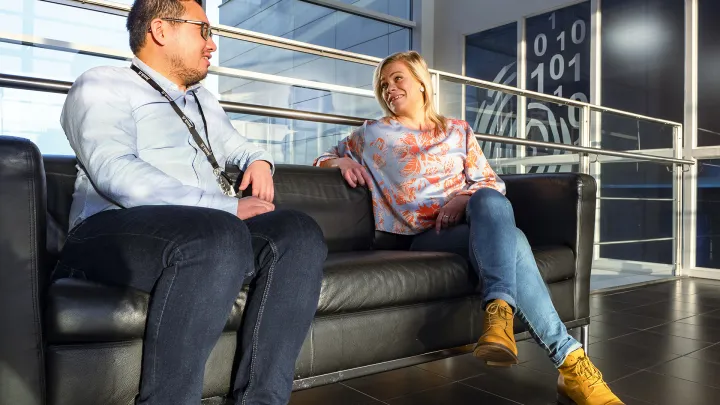 Kaksi henkilöä istuu sohvalla ja keskustelee. 