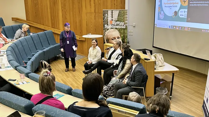 Luentosalissa käynnissä paneelikeskustelu, jossa neljä henkilöä ja yleisö seuraa keskustelua.