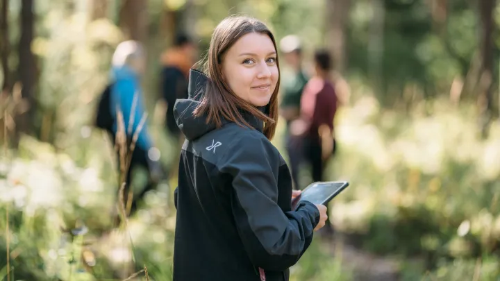 Nainen kavelee metsassa ipadin kanssa