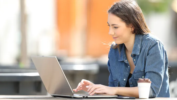 Nainen tietokoneen ääressä kahvikupin kanssa