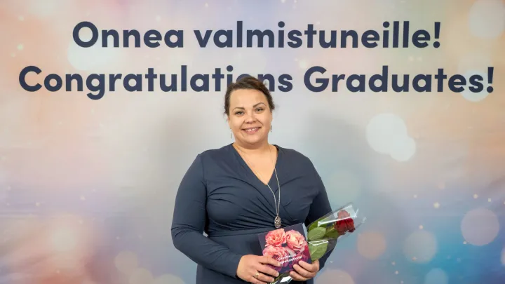 Päivi Toivainen valmistujaisjuhlassa ruusu ja kortti kädessään