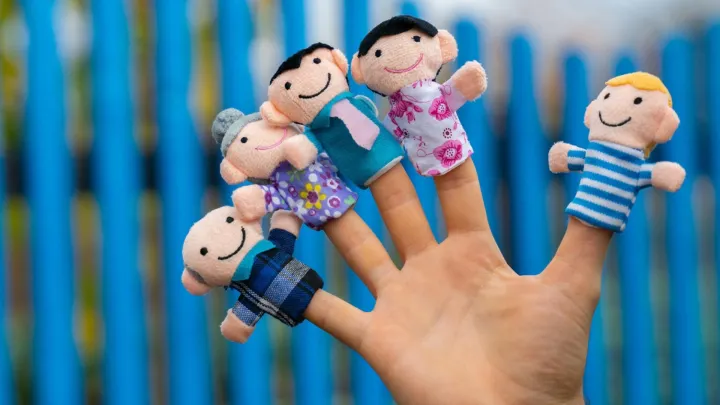 Henkilön käsi, jonka sormenpäissä on pieniä nukkeja.