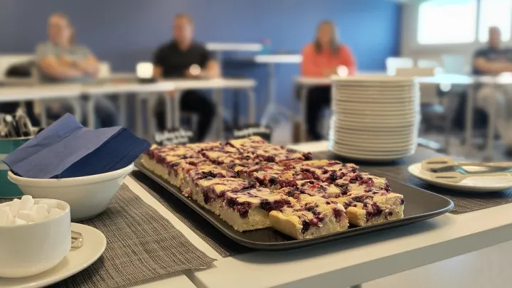 Luokkatilassa esillä tarjotillinen marjapiirakkaa, taustalla istumassa henkilöitä.