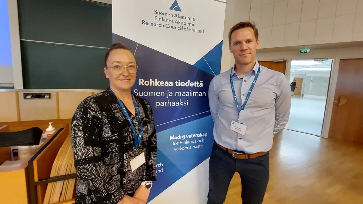 Piritta Asunta ja Mikko Huhtiniemi seisovat Suomen Akatemian rollupin edessä.