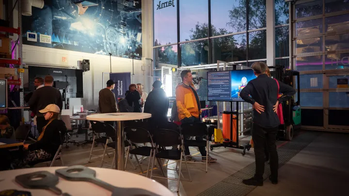 Teknologian laboratorio, jossa hämärä iltavalaistus. Ihmiset katselevat erilaisia teknisiä laitteita.