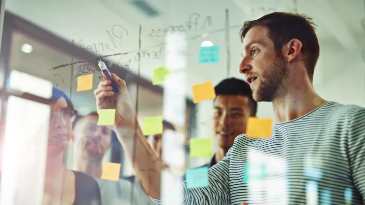 Ryhmä aikuisia työstää ideoita pleksiseinämän äärellä.