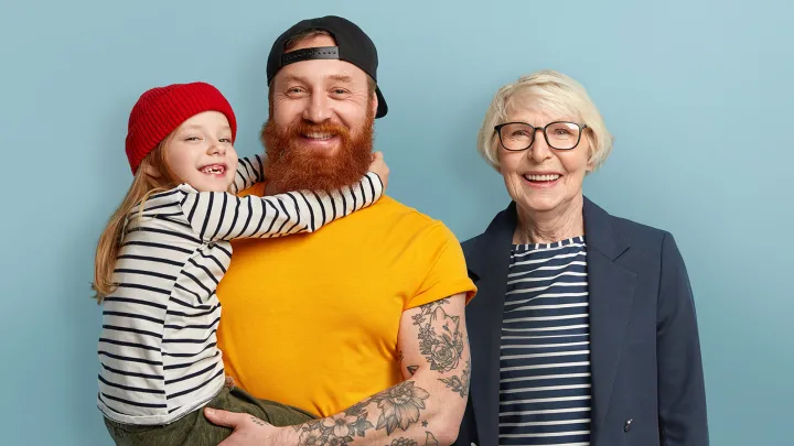 Lippalakkipäinen mies pitää sylissä lasta, vaaleahiuksinen vanhempi nainen vieressä.