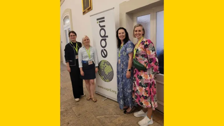 Henkilöitä seisoo EAPRIL-konferenssin roll-upin edessä.