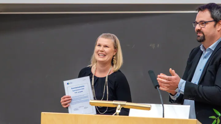 Naishenkilö pitelemässä hymyillen kunniakirjaa.